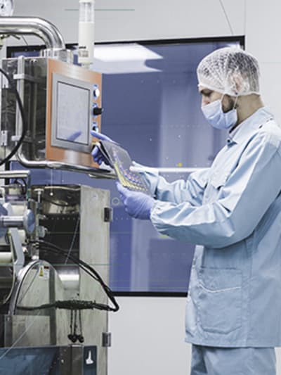 Industrial worker wearing face and head cover works on complex industrial equipment.